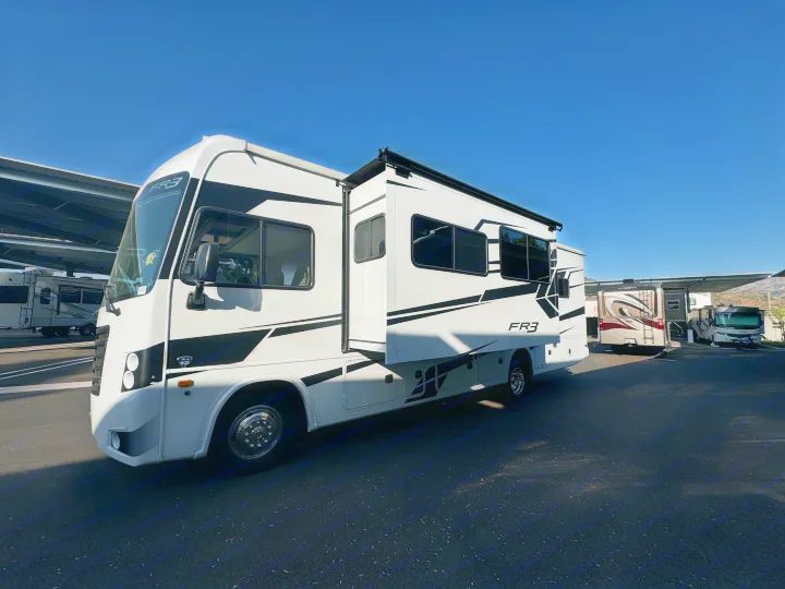 A white Forest River FR3 Class A motorhome, ideal for an rv rental, parked on asphalt with slide-out extended. Other RVs are in the background.. Forest River Fr3 2021
