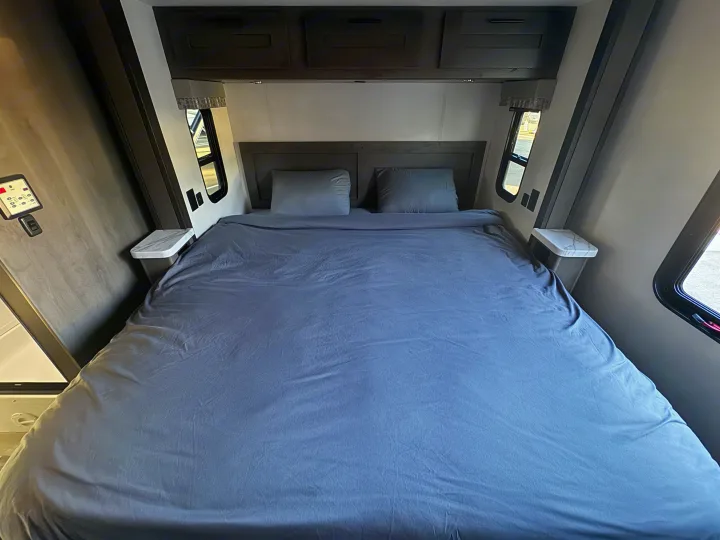 Clean and cozy RV rental bedroom featuring a queen bed with gray linens, overhead cabinets, and side windows.. Forest River Fr3 2021