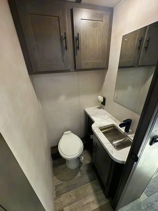Clean RV rental bathroom featuring a toilet, sink vanity with marble top, black faucet, and modern overhead cabinets.. Forest River Fr3 2021