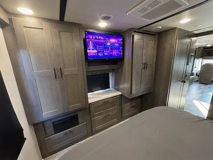 Inside this spacious rv rental, you'll find a modern bedroom with wooden cabinetry, a wall-mounted TV, and a cozy bed.. Forest River Fr3 2021