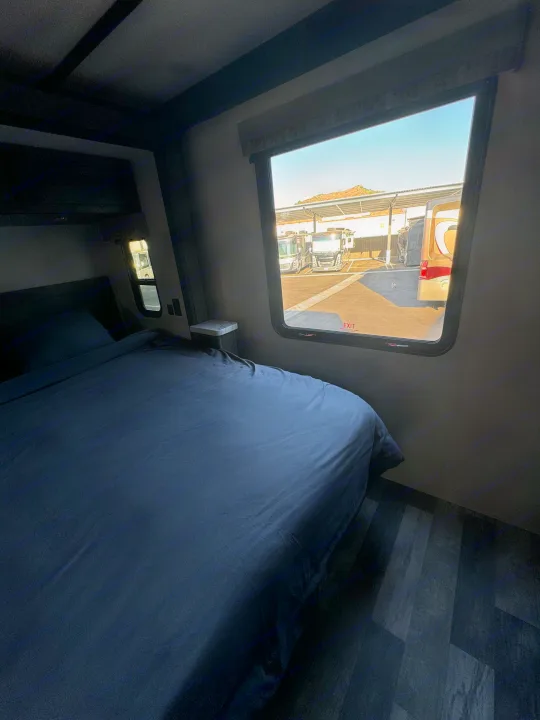 Inside a spacious RV rental bedroom, featuring a dark bed and exterior view of parked motorhomes.. Forest River Fr3 2021