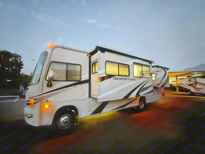 Night shot of a parked Georgetown RV rental with lights on, slide-outs extended, in an RV park.. Forest River Georgetown 2018