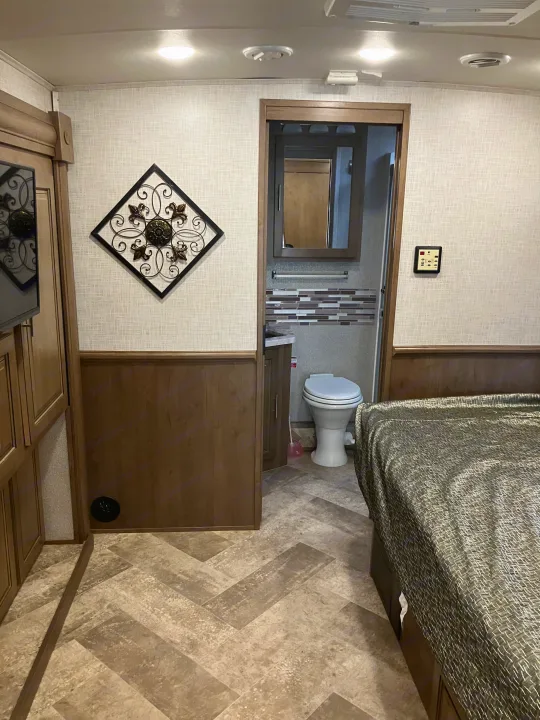RV rental interior: A compact bedroom area with a patterned bedspread, leading to an attached bathroom with a visible toilet.. Forest River GEORGETOWN GT5 2019
