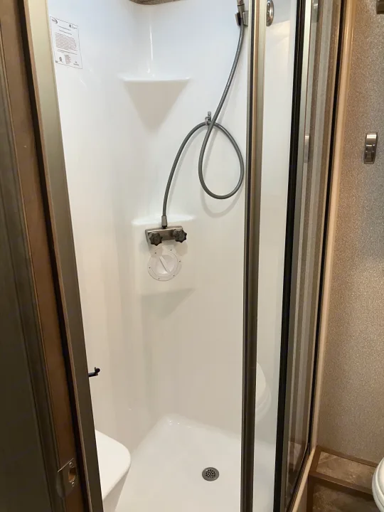 RV rental's bright white, compact shower stall with a handheld showerhead, controls, and floor drain visible.. Forest River GEORGETOWN GT5 2019