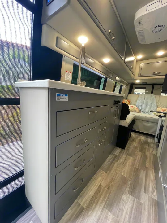 Spacious RV rental interior featuring a modern kitchenette with sink, drawers, overhead cabinets, and comfortable seating.. Holiday Rambler Expedition 2024
