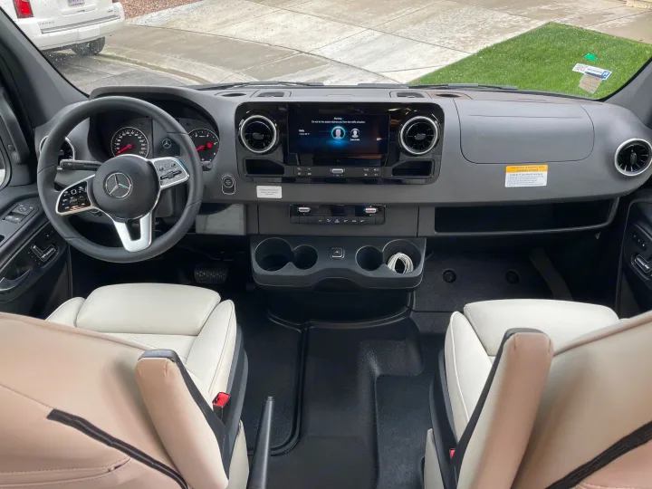 RV rental cockpit view: Mercedes steering wheel, dashboard with infotainment screen, and clean, light-colored front seats.. Holiday Rambler Expedition 2024