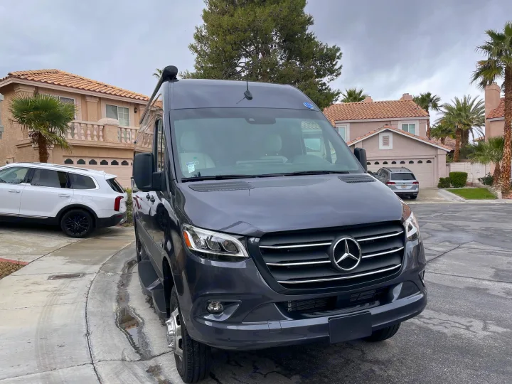 Dark gray Mercedes-Benz Sprinter van, ideal for rv rental, parked on a wet driveway in a residential area.. Holiday Rambler Expedition 2024