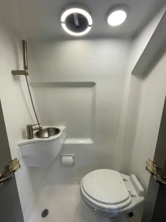 This RV rental wet bath features a compact toilet, wall-mounted sink, and shower in a bright, efficient design.. Holiday Rambler Expedition 2024