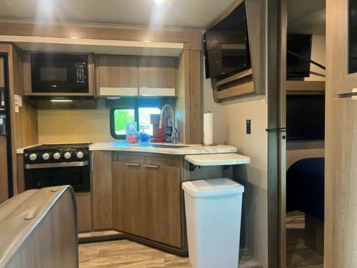 RV rental interior: full kitchen with stove, microwave, sink, plus living/bedroom space with wall-mounted TVs. Compact design.. Grand Design Imagine XLS 2021