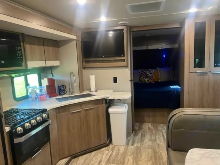 Inside a comfortable RV rental: A well-equipped kitchen, cozy bedroom, and compact dining area are visible.. Grand Design Imagine XLS 2021
