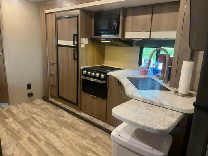 RV rental kitchen interior: features a fridge, stove, microwave, sink, and pull-out counter over wood-look flooring.. Grand Design Imagine XLS 2021