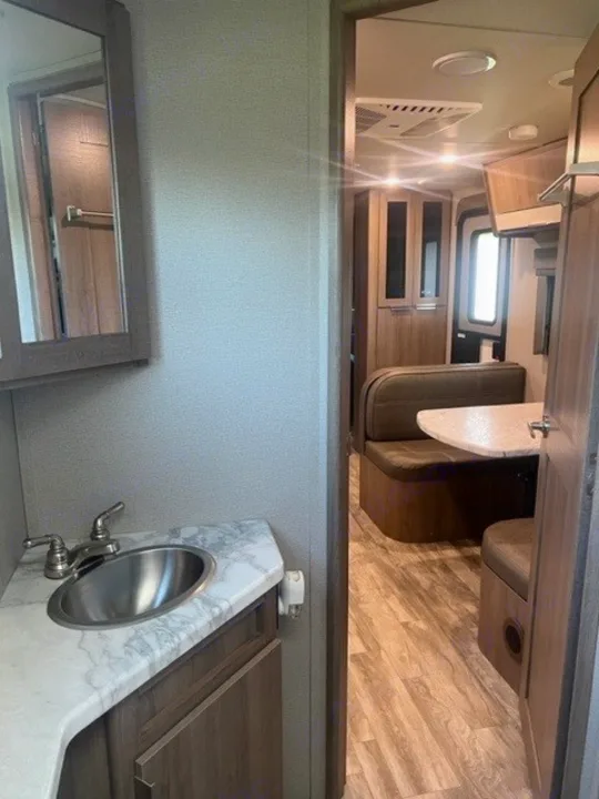RV rental interior features a bathroom vanity with sink & mirror, leading to a cozy dinette area.. Grand Design Imagine XLS 2021