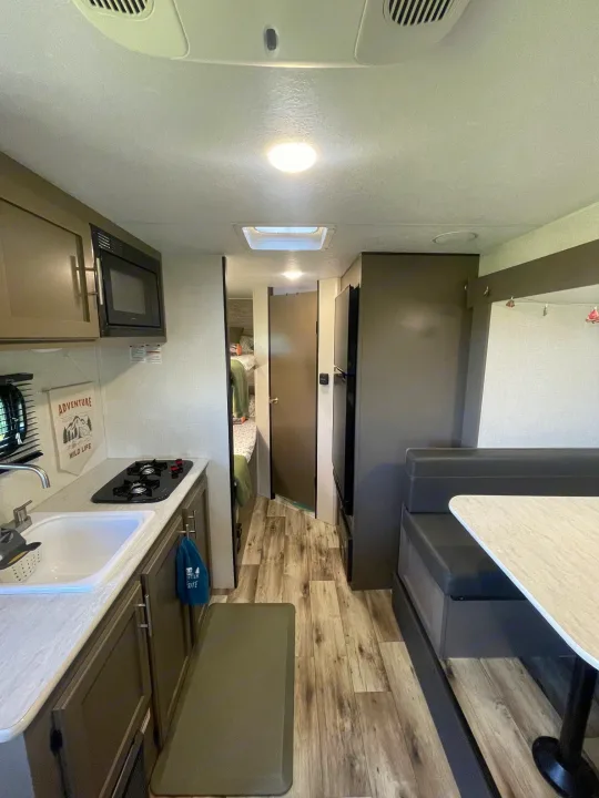 RV rental interior: compact kitchen, dining booth, and bunk beds offer a functional space for travel.. KZ SPORTSMEN CLASSIC 191BHK 2024