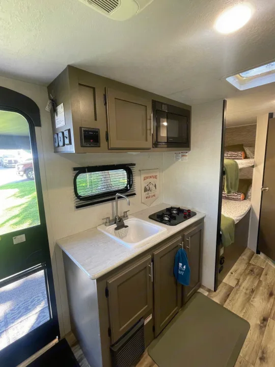 Modern RV rental interior with kitchen sink, stovetop, microwave, and bunk beds. Bright, functional living space.. KZ SPORTSMEN CLASSIC 191BHK 2024