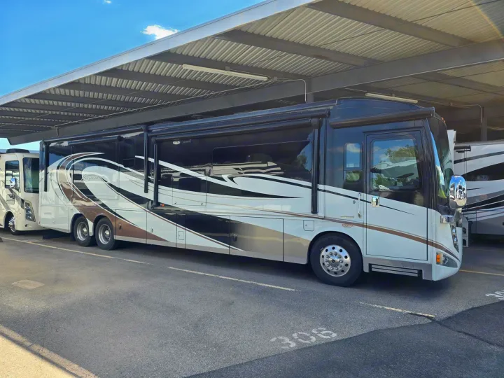 A sleek, large black & white RV rental, with slide-outs extended, under covered storage. Parked next to another RV.. Winnebago Ellipse 2016