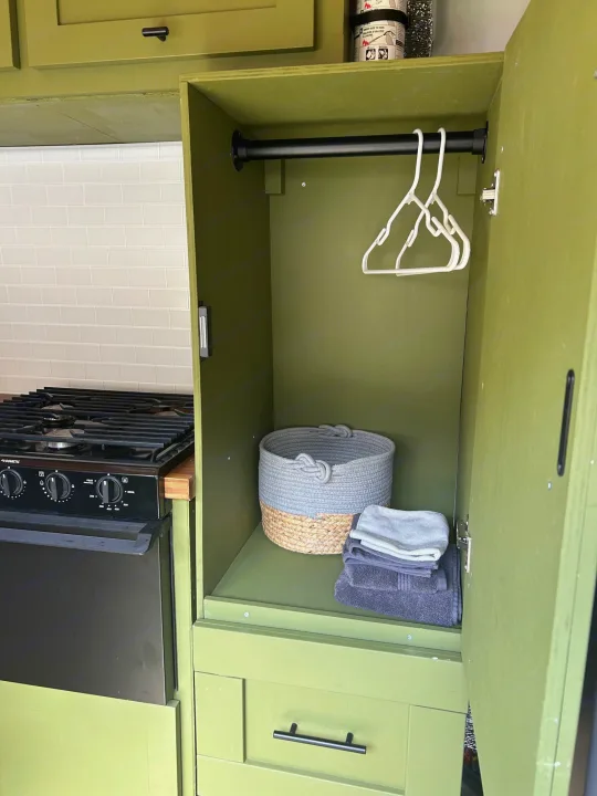RV rental interior: organized olive green cabinetry, a stovetop kitchen, and a tidy wardrobe with hangers, basket, and towels.. Ford Transit 2019