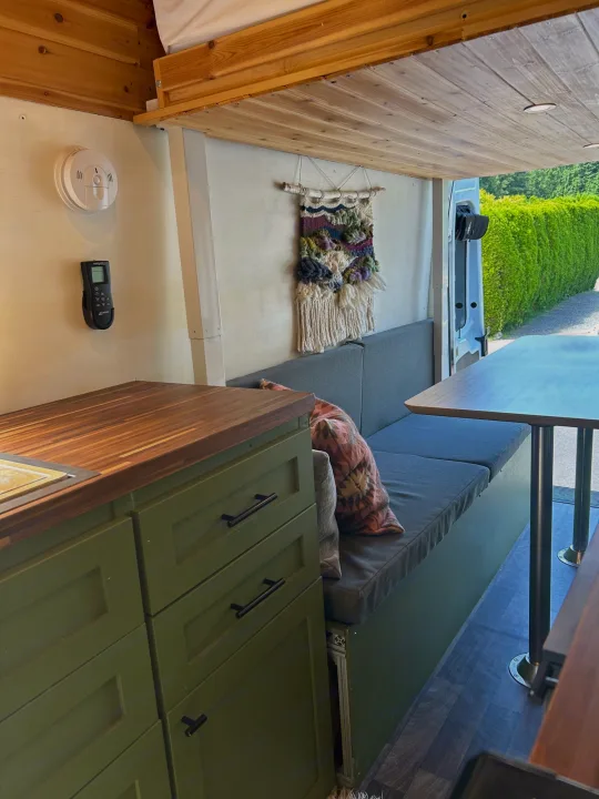 Inside a custom rv rental: green kitchenette cabinets, wood counter, comfy bench seating, and dining table.. Ford Transit 2019