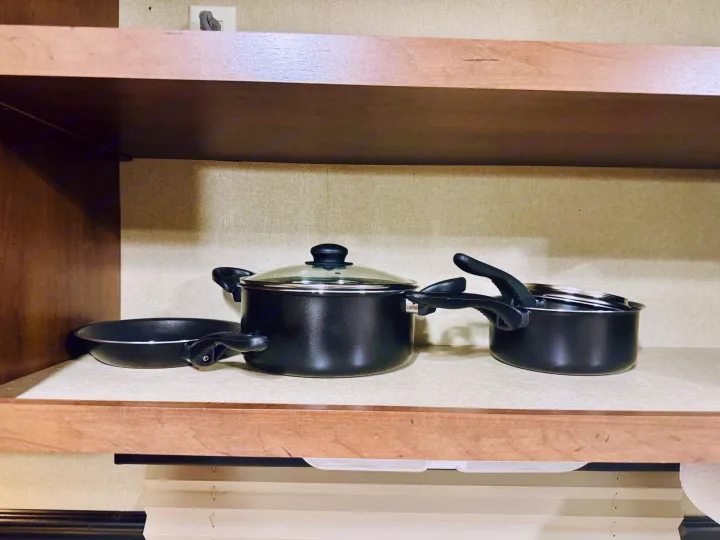 Cookware storage in an RV rental: black pots & pans neatly arranged on a wooden shelf with a glass lid visible.. Aspen Trail Aspen Trail Trailer 2014