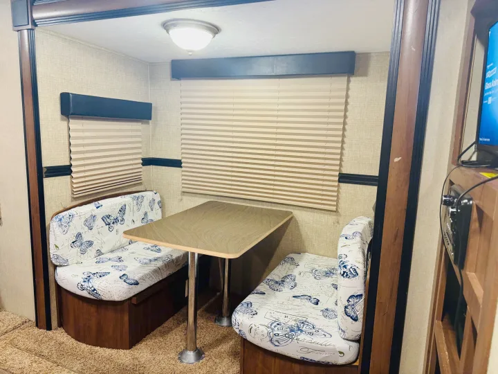 RV rental dinette area featuring butterfly-patterned cushions, a central table, and window blinds. Cozy interior space for dining.. Aspen Trail Aspen Trail Trailer 2014