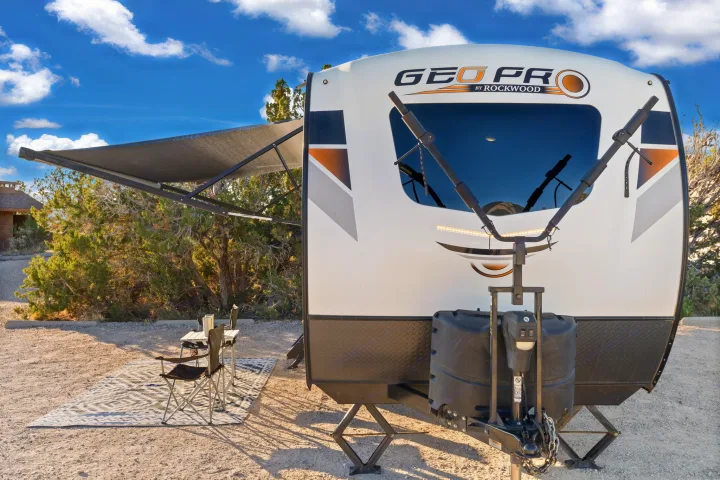 This inviting RV rental is set up at a sunny campsite with an extended awning, chairs, and a table for outdoor living.. Rockwood G19QB 2021