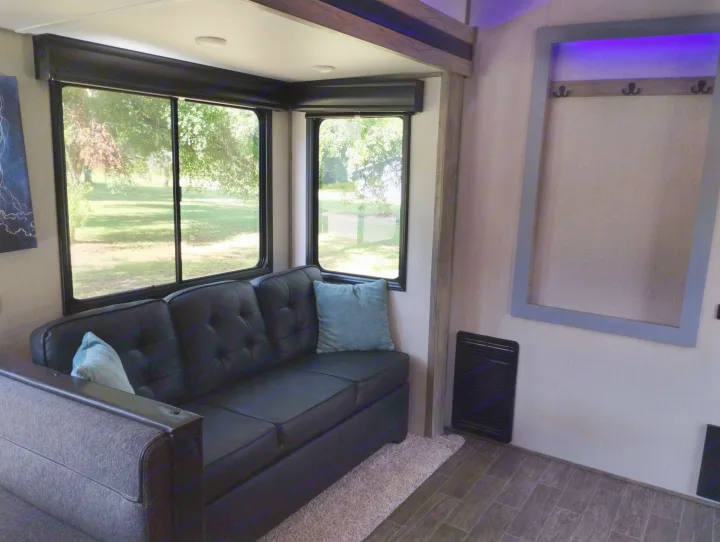 Inside a comfy RV rental: A dark sofa, bright windows overlooking trees, and a wall-mounted storage area with hooks.. Forest River Cherokee Arctic Wolf 2021