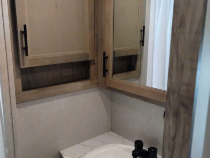 RV rental bathroom with compact vanity, sink, mirror medicine cabinet, and open storage. Modern design details.. Forest River Cherokee Arctic Wolf 2021