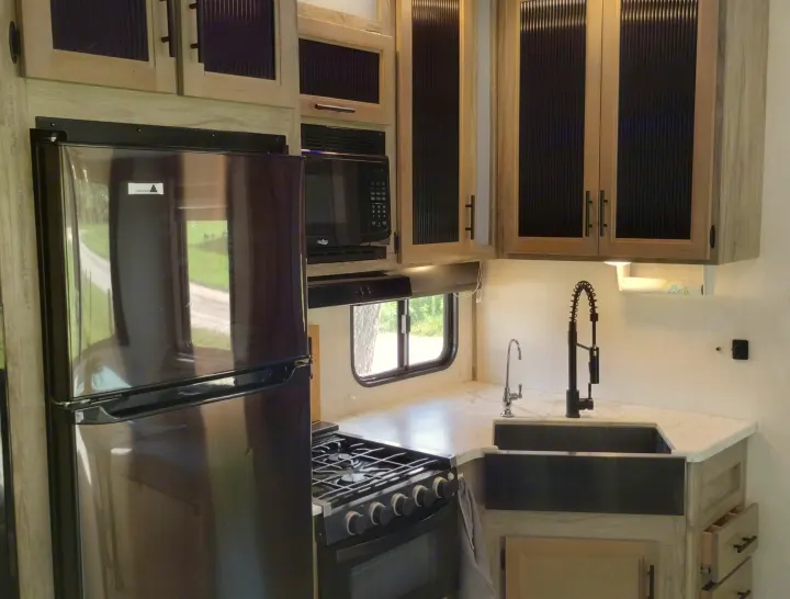 Spacious RV rental kitchen featuring black fridge, stove, microwave, modern sink, and light wood cabinetry.. Forest River Cherokee Arctic Wolf 2021