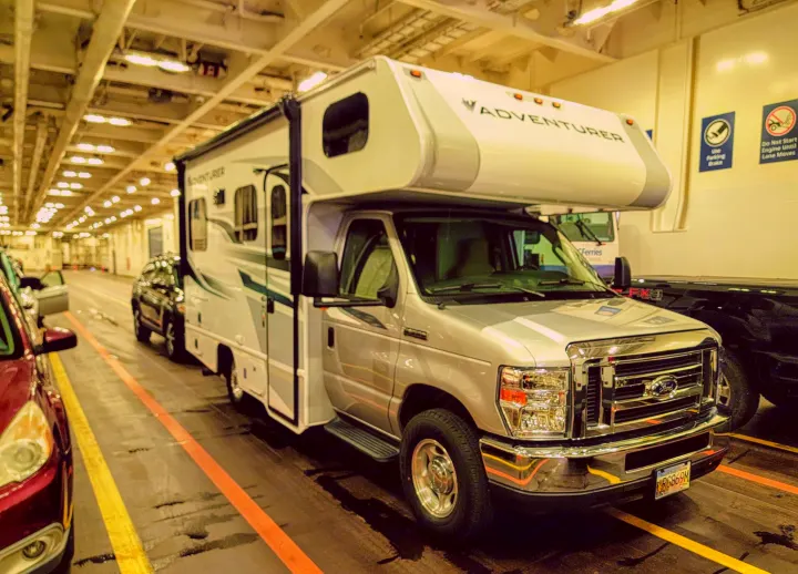 An RV rental, likely a Ford Adventurer model, parked on a car ferry deck with striped lanes and other vehicles.. ALP Adventurer 19RD 2021