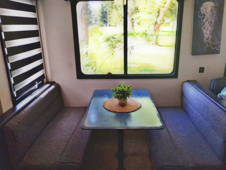 RV rental: a cozy dinette with bench seating, a table with a plant, and a large window showcasing a lush outdoor view.. Forest River Cherokee Arctic Wolf 2021