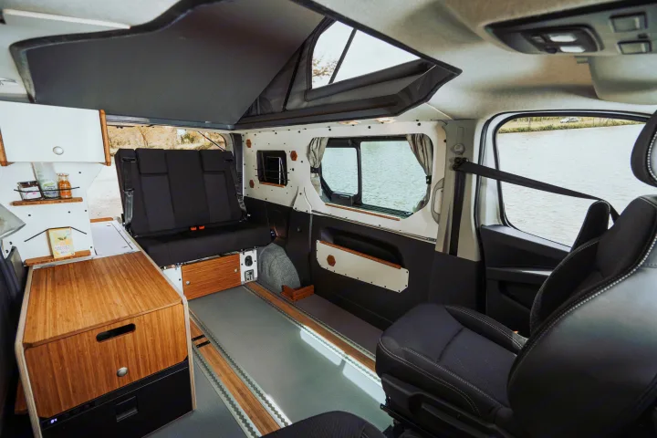 Spacious RV rental interior with pop-top roof, flexible seating, and kitchen area, offering serene water views.. Renault TRAFIC 2023