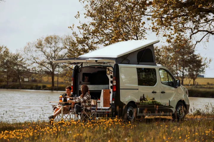 A couple enjoys an rv rental pop-top camper van by a lake. Perfect for peaceful outdoor living and adventures.. Renault TRAFIC 2023