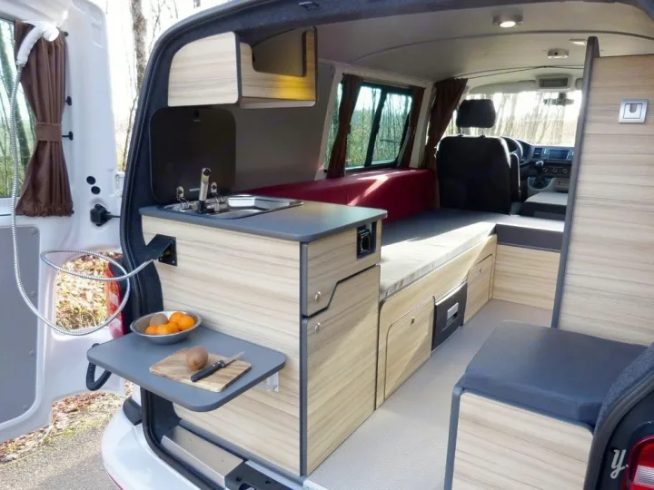 Compact RV rental interior featuring a kitchenette, fold-out table, bed, and rear shower.. opel L'OTAGO (Caen) 2024