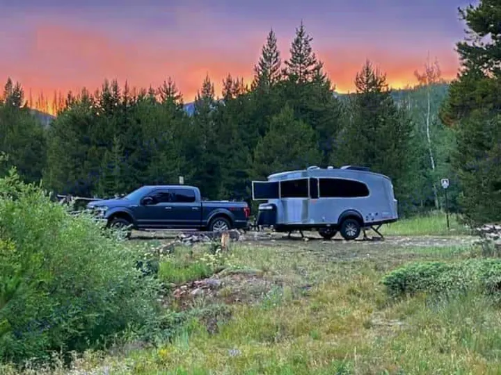 An RV rental pickup truck and sleek travel trailer at a wooded campsite, bathed in sunset hues.. Airstream Basecamp 2023