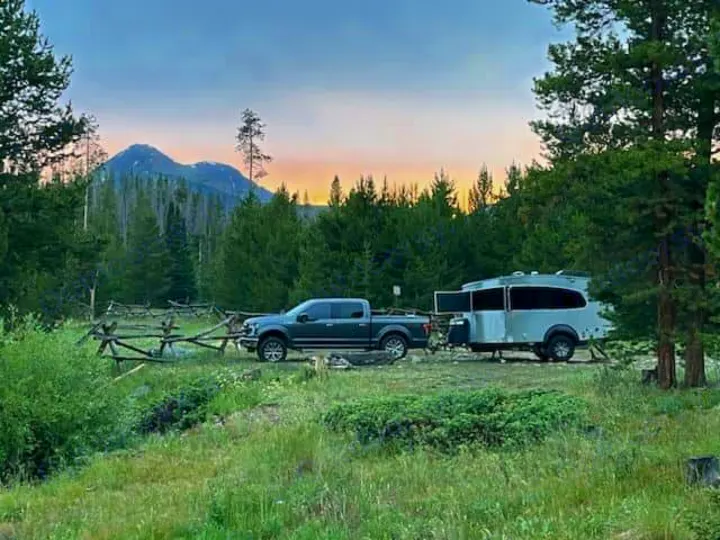 Truck and RV rental trailer parked in a scenic mountain setting with pine trees at sunset, ideal for outdoor camping.. Airstream Basecamp 2023