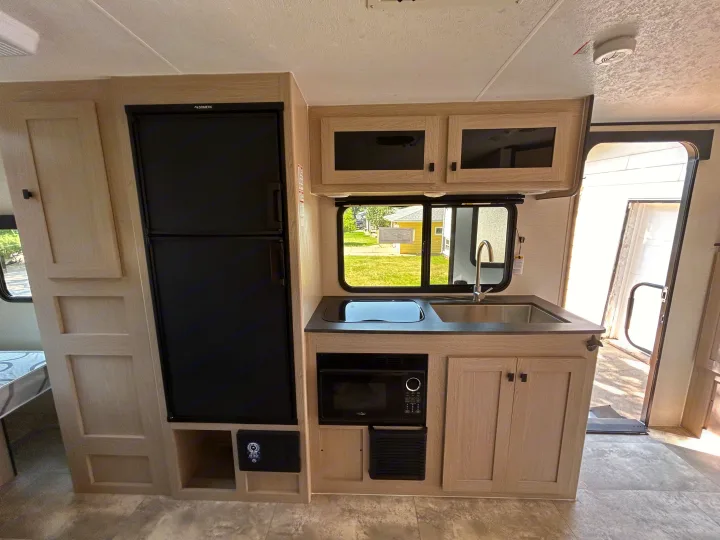 Inside a modern RV rental: kitchenette with fridge, sink, microwave, and cabinets. Ready for your camping adventure.. Coachmen Apex Nano 2023