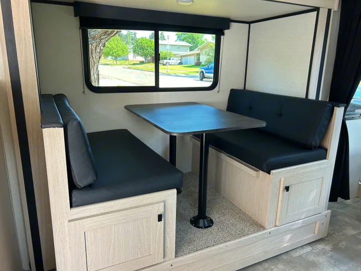 Bright RV rental dinette with black benches, light wood, and a large window offering an outdoor view.. Coachmen Apex Nano 2023