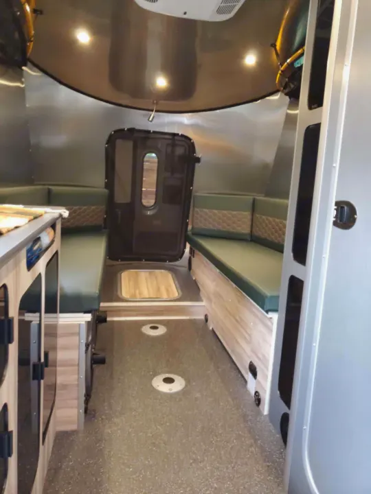 Inside an RV rental: features facing green bench seats, a counter, and a dark door. Bright, functional camper interior.. Airstream Basecamp 2023