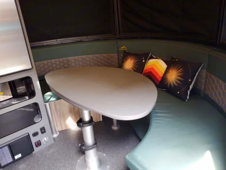 Explore this comfy RV rental dinette! Curved green seating, adjustable table, pillows & control panel for your travels.. Airstream Basecamp 2023