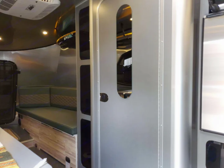 Modern RV rental interior with green cushioned seating, wood-look base, and sleek silver walls.. Airstream Basecamp 2023