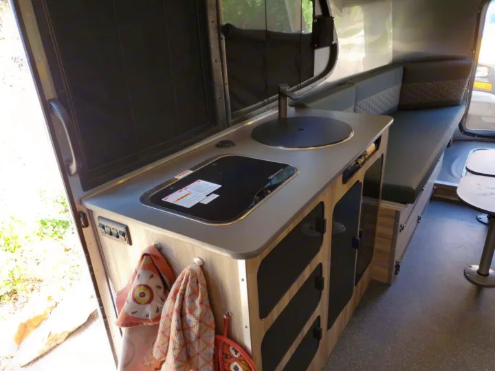 RV rental: This interior shows a compact kitchen with a covered sink, cooktop, storage cabinets, and a dinette.. Airstream Basecamp 2023