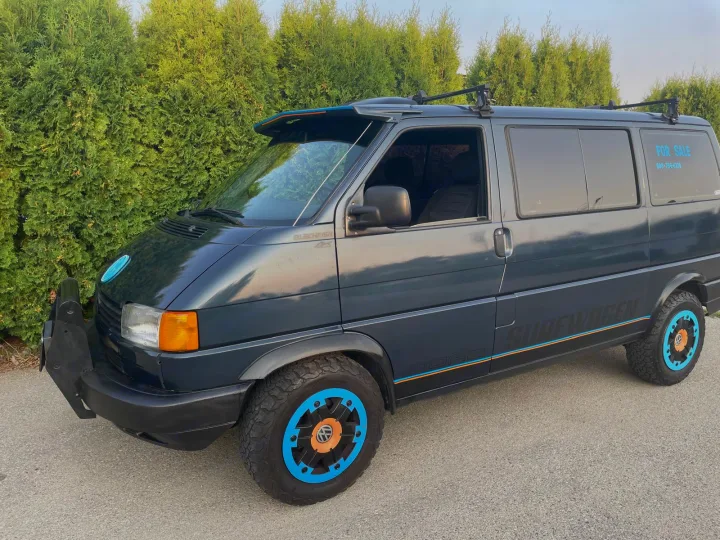 Customized dark grey VW "SURFWAGEN" van with off-road tires and roof rack, ready for an RV rental adventure.. Volkswagen eurovan 1996