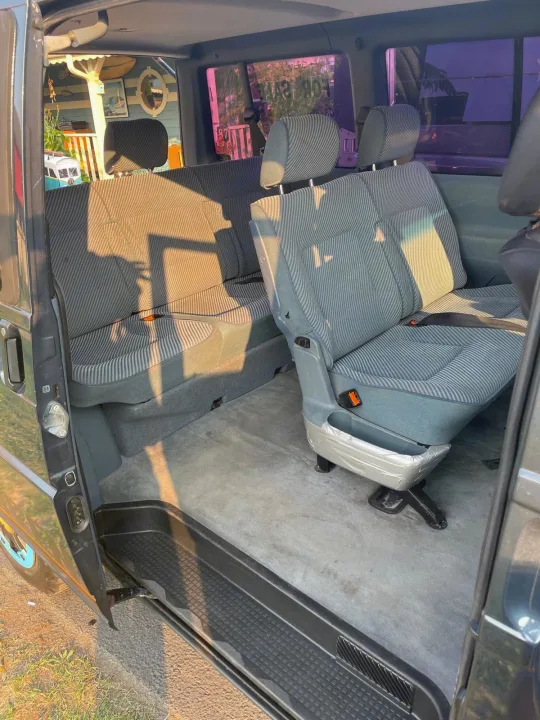 RV rental van interior: rear seating with striped upholstery, bathed in sunlight. Side door open, revealing comfortable travel space.. Volkswagen eurovan 1996