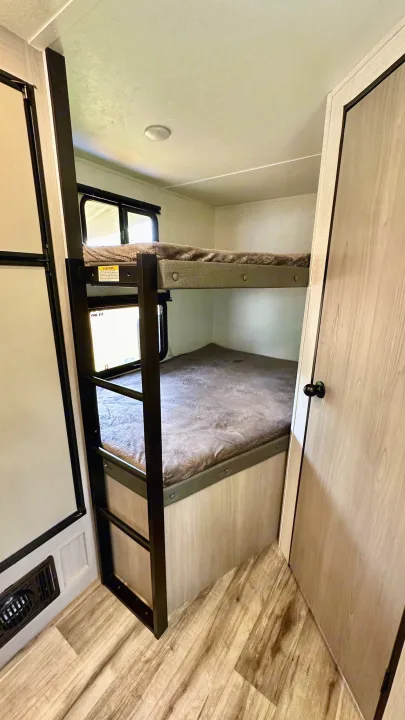 View of cozy bunk beds in an RV rental, featuring a ladder and two sleeping levels with windows, ideal for compact travel.. Dutchmen Coleman Light 2023
