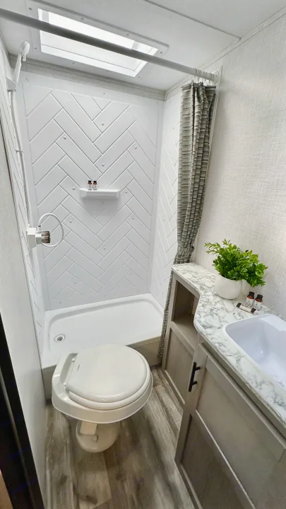 Step inside a functional RV rental bathroom featuring a white shower with a herringbone pattern, toilet, and vanity.. Dutchmen Coleman Light 2023