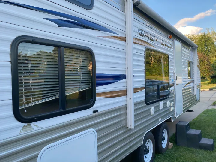 Side view of a "Grey Wolf" travel trailer RV rental, showing its windows, awning, and entrance steps on a sunny day.. Forest River Cherokee Grey Wolf 2012