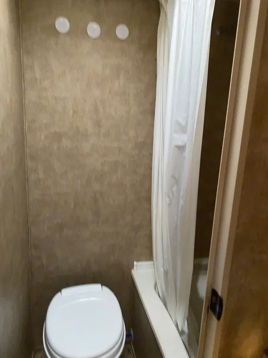 Inside an RV rental's compact bathroom: white toilet, shower with curtain, and overhead lights. Functional and practical.. Forest River Cherokee Grey Wolf 2012
