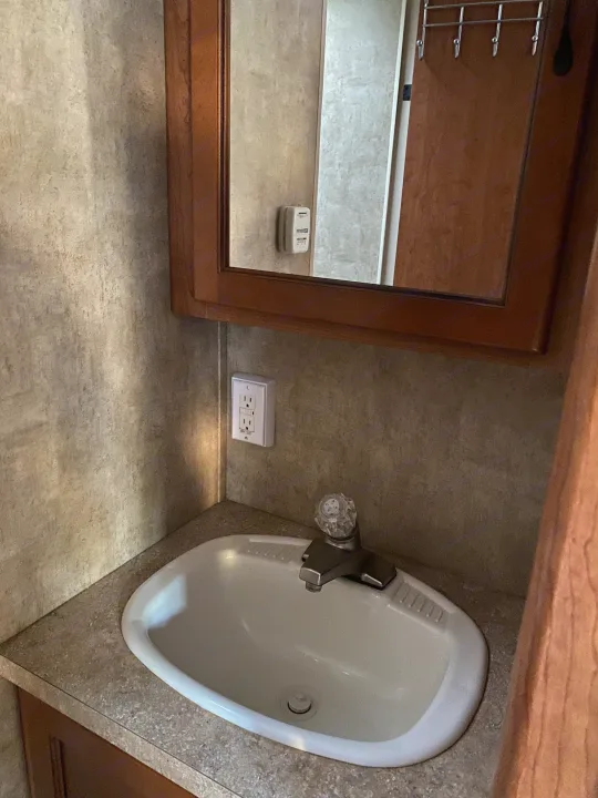 RV rental bathroom essentials: compact sink, faucet, mirror, and wall outlet. Functional space for travel.. Forest River Cherokee Grey Wolf 2012