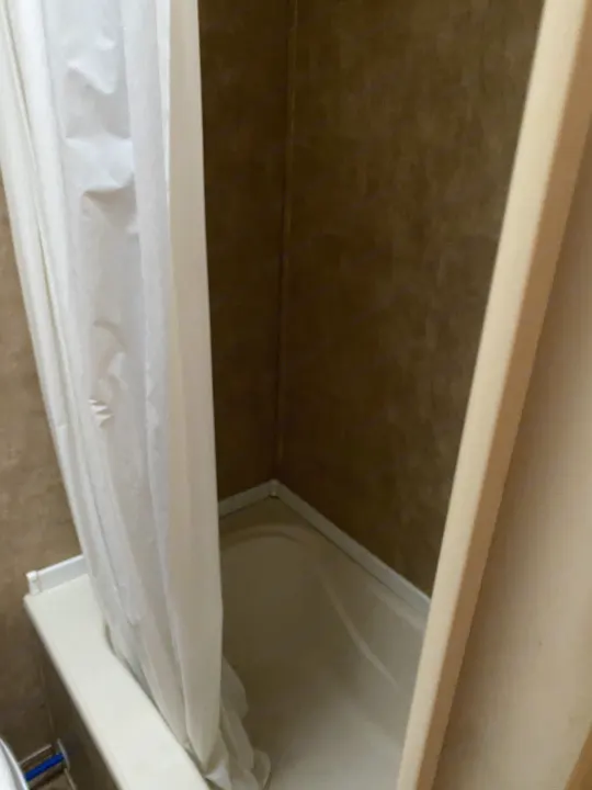 Compact shower and bathtub area inside an RV rental bathroom, with a white shower curtain drawn.. Forest River Cherokee Grey Wolf 2012