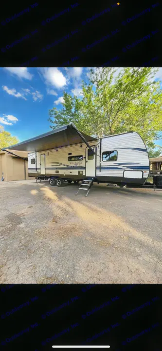 Spacious travel trailer RV rental parked outdoors with awning extended under a blue sky.. Keystone Springdale 2021