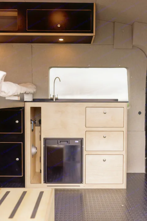 This RV rental shows a modern camper van kitchen with a sink, faucet, refrigerator, and light wood cabinetry.. Ford Transit 2020